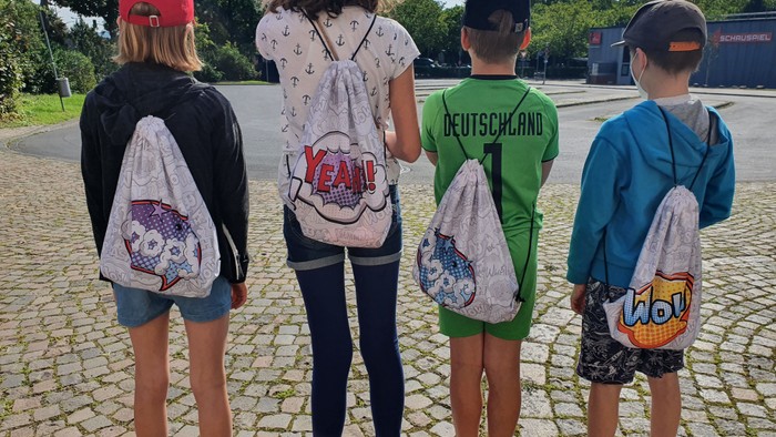 Vier Kinder laufen weg, jeder mit einem Rucksack mit bunten Mustern.
