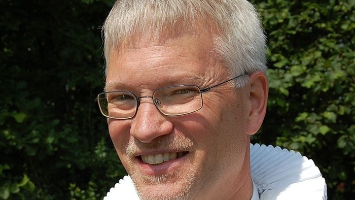 Mand med hvid krage og briller.