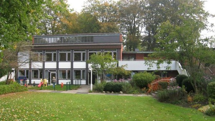 Das Bild zeigt ein modernes Gebäude mit großen Fenstern und einer grünen Rasenfläche davor.