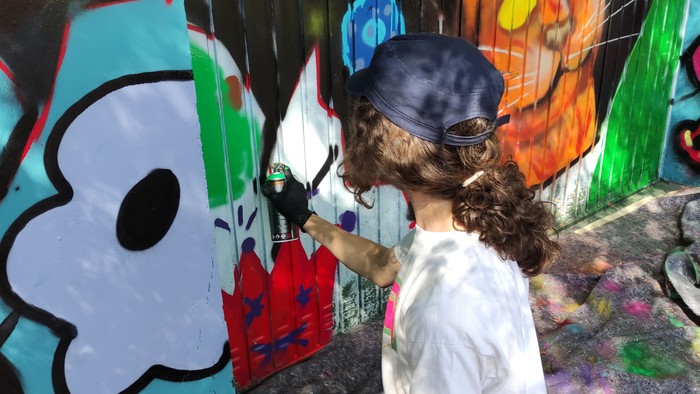 Ein Kind mit einer blauen Mütze sprüht eine bunte Wand.