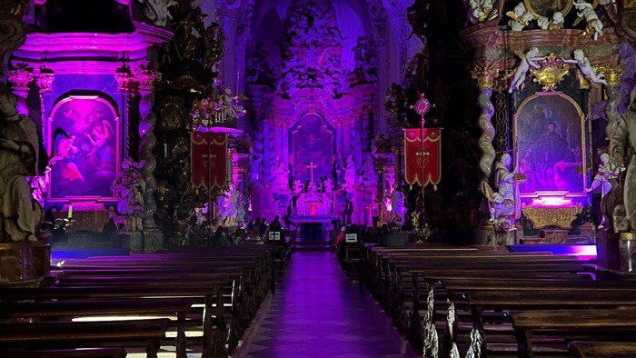 Kircheneingang mit lila Beleuchtung und Holzbänken