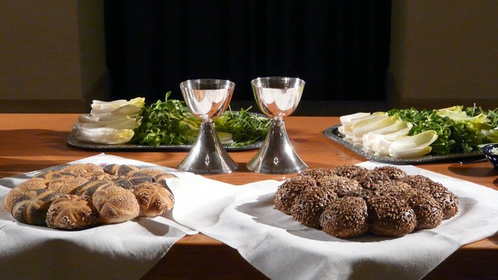 Auf dem Tisch stehen zwei Schalen mit Brötchen, zwei Gläser und zwei Salate.