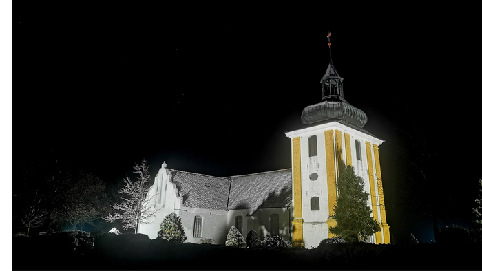 En belyset kirke med tårn og juletree i forgrunden