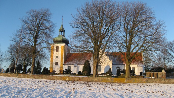 En kirke med tårn og rødt tag i sneklædt landskab