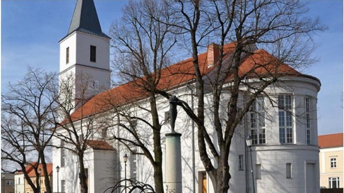 Weißes Kirchengebäude mit rotem Dach und Turm, umgeben von kahlen Bäumen