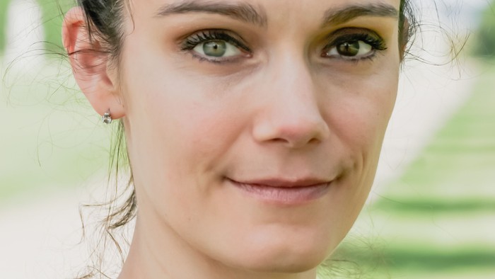 En ung kvinde med grønne øjne og hår i et bundbånd, smiler og ser i kameraet.