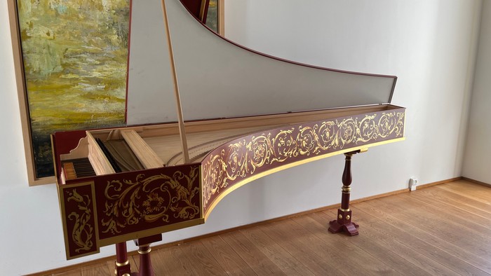 En smuk hvid fløjtepiano med udsmykning i et rum med guldtone maleri på væggen.