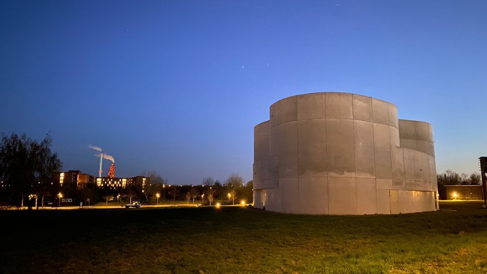 En stor, rund betonstruktur belyset ved natten, omgivet af græs og træer