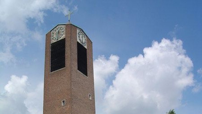 Hoher Backsteinuhrturm in der Nähe einer Straße mit Autos.