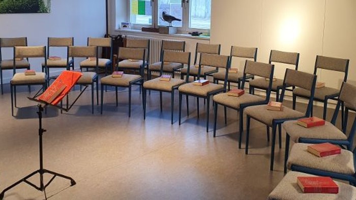 Ein Raum mit Stühlen und einem Klavier, ein Bild an der Wand, ein Fenster mit Blick auf Bäume.