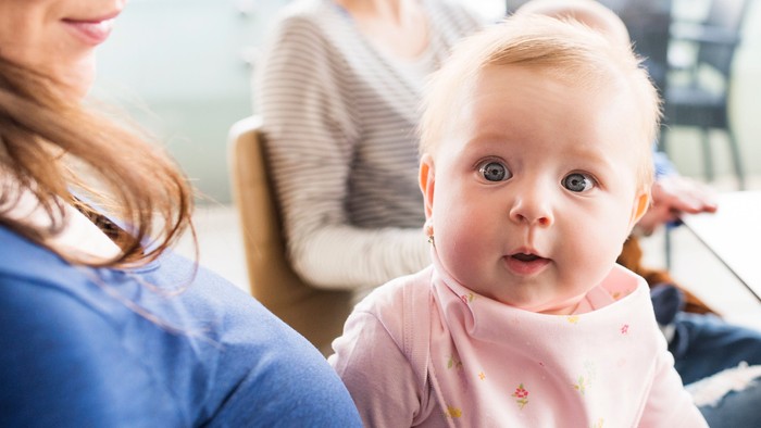 Eine Frau hält ein Baby, während eine andere Frau im Hintergrund steht und zusieht.