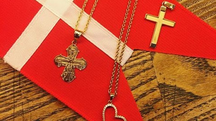 Tre halsbånd med kors og hjerte udsmykninger på rød og hvid stoff over træ