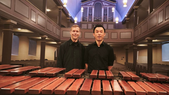 Zwei Männer stehen in einer Lagerhalle mit Holzstämmen