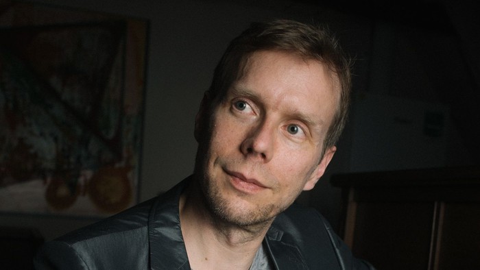 Mann in dunklem Anzug spielt Klavier und lächelt.