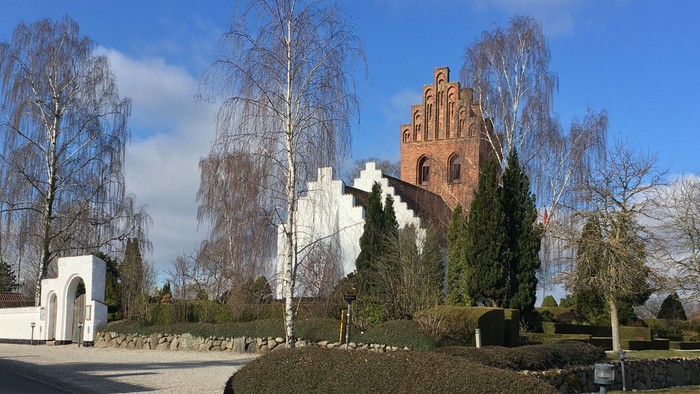 En gammel kirke med tårn og en mur af sten med buske foran