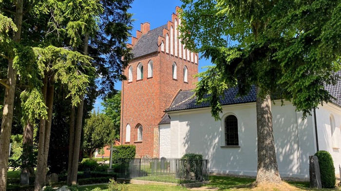 En lille kirke med tårn og murstensvægge, omgivet af træer og en græsplæne