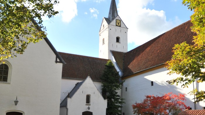 En hvid kirke med tårn og træer med faldne blade.