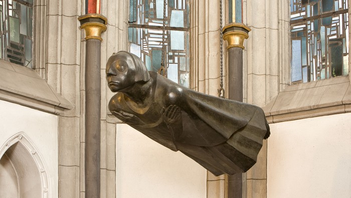 Die Statue eines schwebenden Menschen vor einem Gebäude mit Säulen und großen Fenstern.