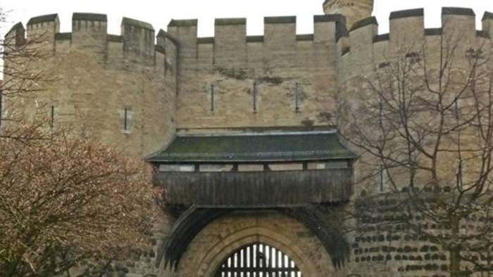 Ein alter Steinbogen mit einem Holzdach, umgeben von Bäumen und Gebäuden