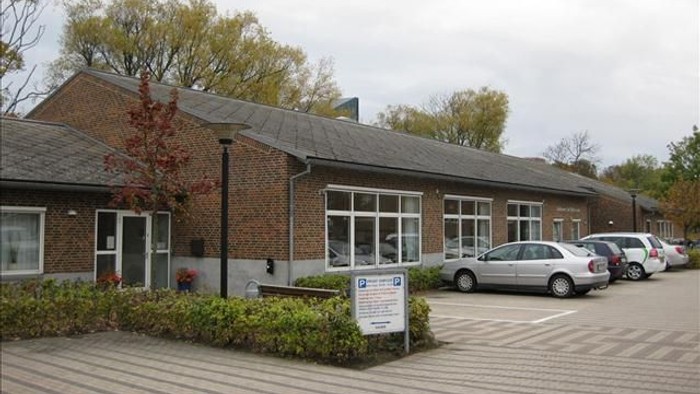 En lav, længgende bygning med røde mursten og store vinduer, med flere biler parkeret foran