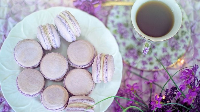 En kaffekop og en kage med lilla macarons på en hvid plate.