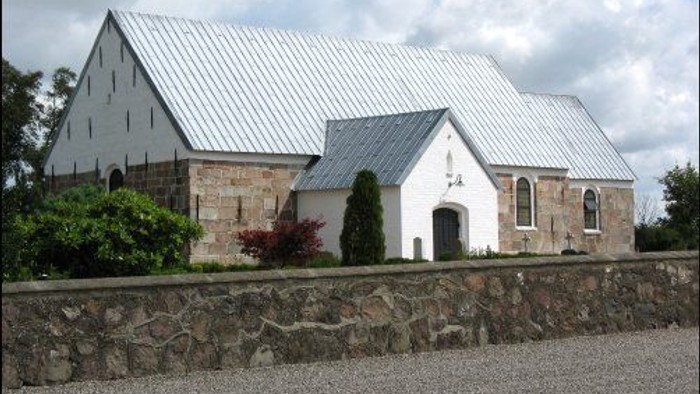 Et lille, hvidt kapel med metaltag og stenmur.