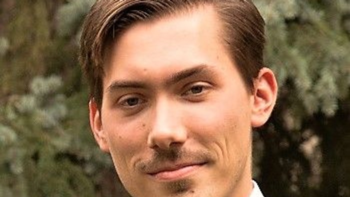 Junger Mann im Anzug mit Krawatte vor grünem Hintergrund.