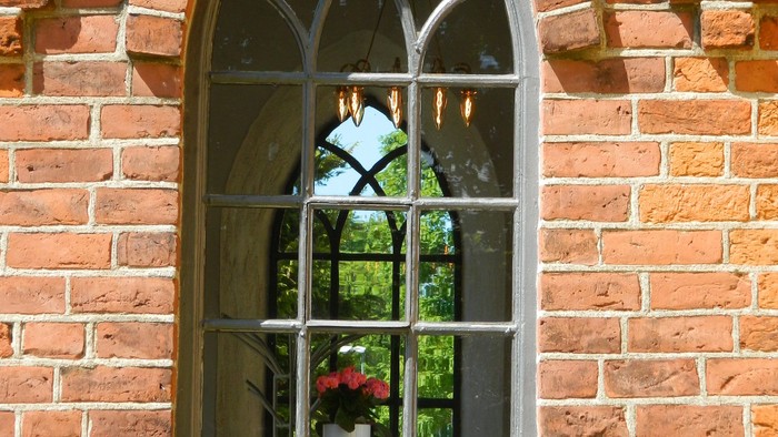 Rudt mursten med bueformet vindue og blomster.