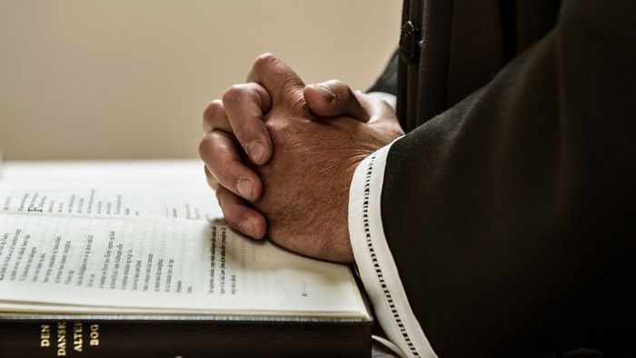 En person med sammenflettede hænder sidder foran en åben bog.