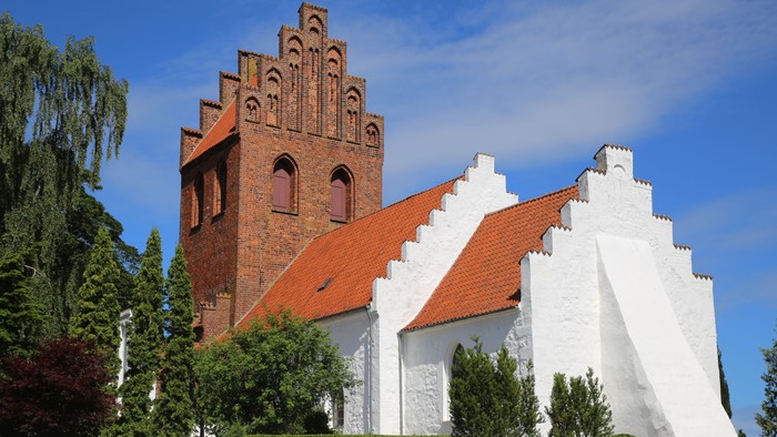 Et rødt teglmurstens tårn og et hvidt kapel med røde tag i en park