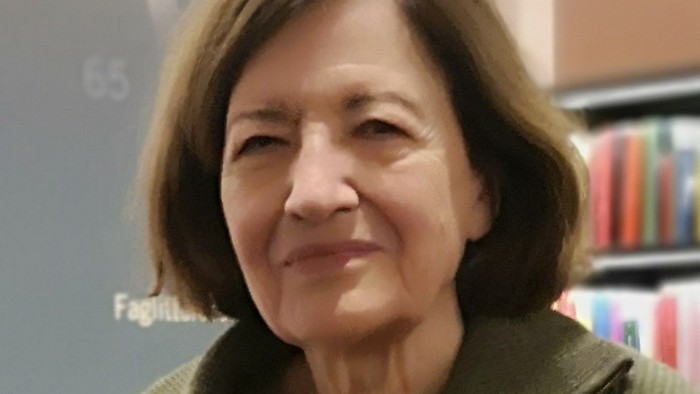 En kvinde med kort, brunt hår og en grøn pullover står i en boghandel.