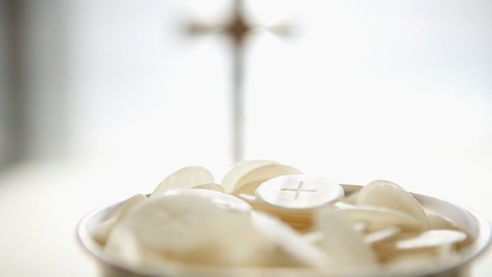 En skål med hvide hostier og en korsformet stang i baggrunden
