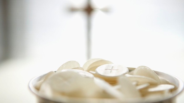 En skål med hvide hostier og en korsformet stang i baggrunden