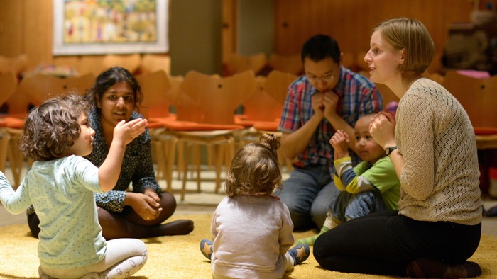 En gruppe af voksne og børn sidder på gulvet og spiller et spil.