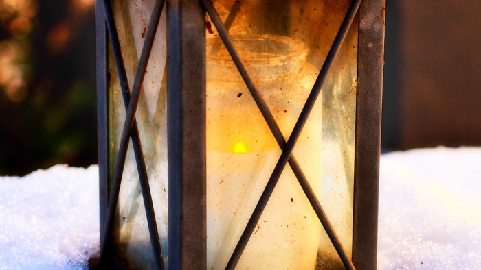 Eine alte Laterne leuchtet warm vor schneebedeckter Kulisse und wirft sanftes Licht durch das vereiste Glas.