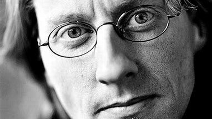En svart-hvid portrætfoto af en mand med briller og kort hår.