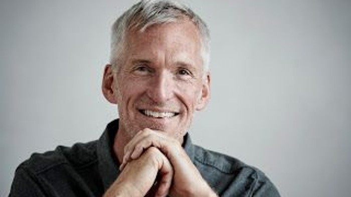 En glade, eldre mand med grå hår og mørke klæder.