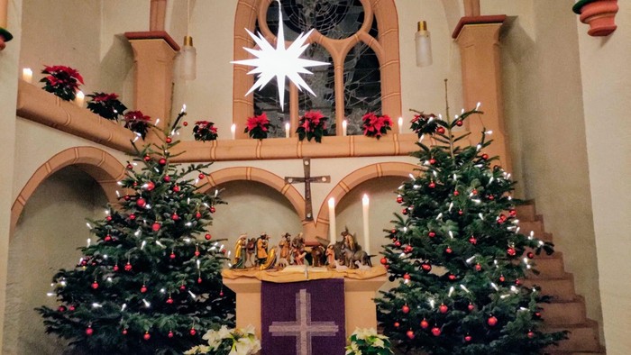 Kirche weihnachtlich geschmückt mit zwei Bäumen und einer Krippendarstellung.