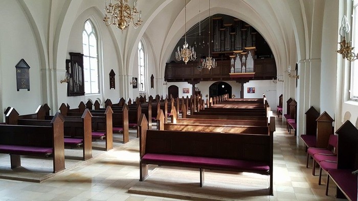 Indre del af kirke med træbænke og hængende lygter