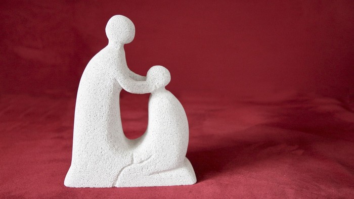 Die Skulptur zeigt eine sitzende Person, die ein Kind im Arm hält.