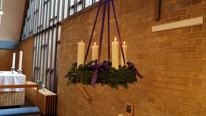 Krystallysekrone med stearinlys og grønt hænger i et stort rum med høje lofter og murstensvægge.