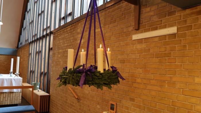 Hængende stearinlysholder med grønne planter og lilla sløjfer i en murstensbygning.