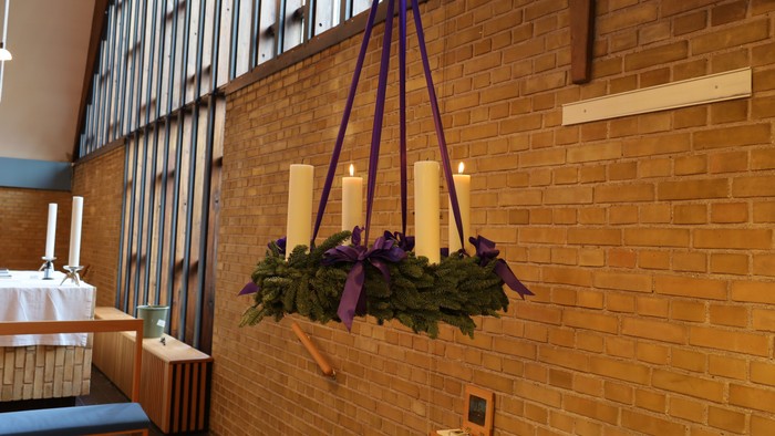 Krone med stearinlys og grønne planter hænger i en murstensbygning.