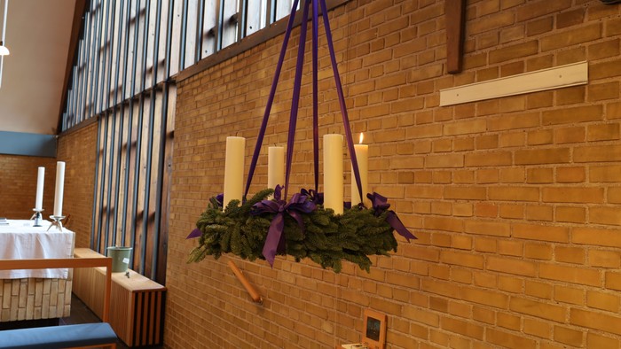 Hængende stearinlysarrangement med grønt og lilla bånd i et rum med murstensvægge.