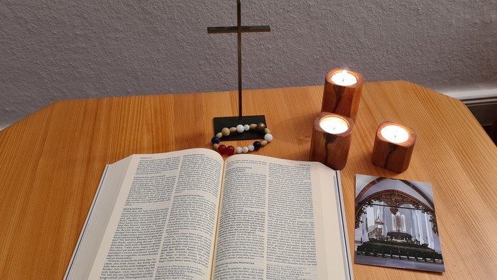 Offene Bibel auf Tisch mit Kreuz und Kerzen