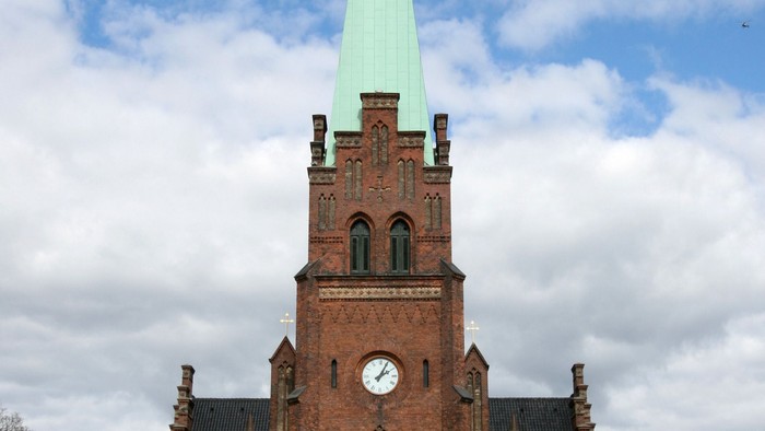 Røde kirke med højt tårn og grøn spire.