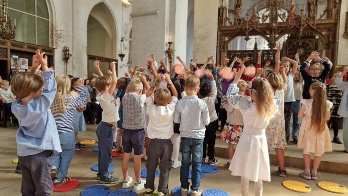 Kinder tanzen in einem großen Raum mit Erwachsenen.