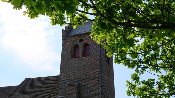 En kirke med tårn og bjælker, delvis skjult af træer