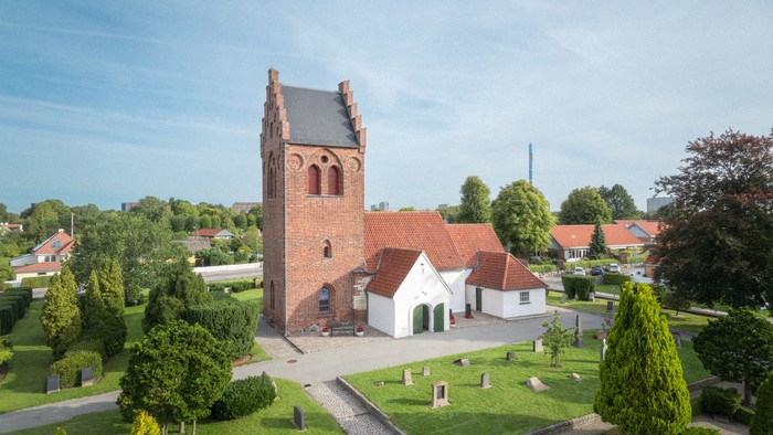 En lille kirke med tårn og gravplads i et præget landskab