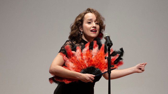 Eine Frau singt leidenschaftlich in ein Mikrofon und hält einen Fächer.